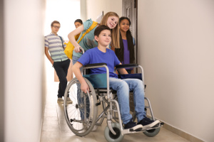 Adolescents dans un couloir d'école, une fille poussant un garçon en fauteuil roulant.