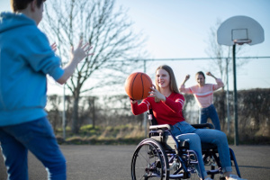 rounded-image Trois jeunes dont une adolescente en fauteuil roulant jouant au basket